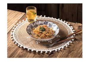 Detail of round jute placemat featuring white tassel fringe and rustic weave on wood table