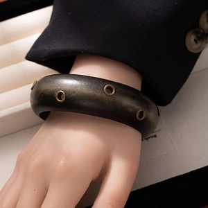 Detail view of a vintage wide wooden bangle featuring bronze eyelet metal decorations