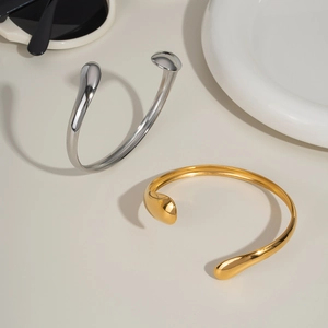 Detailed view of polished wave open bangles in gold and silver stainless steel finishes