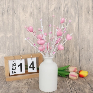 Détail de tiges de baies en forme de cœur rose dans un vase blanc avec calendrier