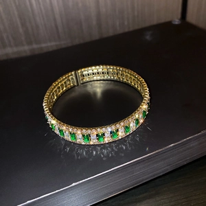 Macro view of gold luxury bracelet featuring emerald green gems and white crystal stones