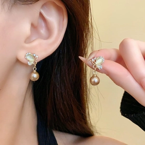 Boucles d'oreilles papillon dorées avec perles et ailes chatoyantes portées par un mannequin