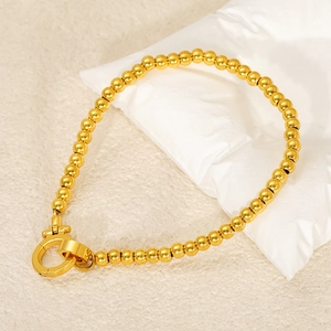 Close-up of gold stainless steel bead chain with horseshoe OT clasp on cream fabric