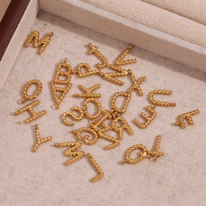 Macro shot of 18K gold plated mini twisted letter pendants on a textured cream fabric