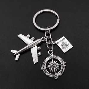 Travel theme keychain with silver airplane, passport charm and compass on black background