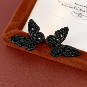 Macro shot of black butterfly stud earrings with rhinestones on brown velvet box