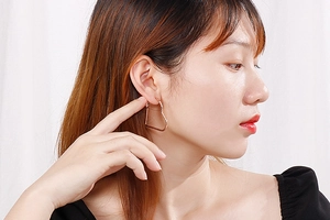 Gros plan d'une boucle d'oreille créole en forme de cœur en or rose portée par un modèle