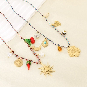 Detail of colorful woven necklaces with gold sun, heart and cherry charms on beige background