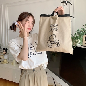 Detail of khaki canvas tote bag featuring lucky bear embroidery and black webbing strap