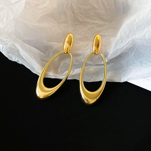 Macro shot of large hollow oval gold earrings on white paper texture with black background