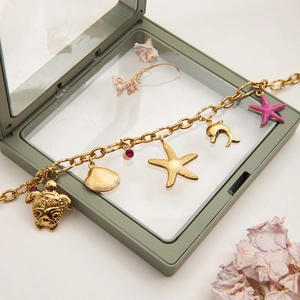 Detail of a gold ocean-themed bracelet with starfish and shell charms on a jewelry box