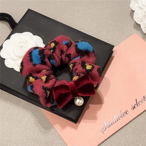 Red knit leopard print scrunchie with velvet bow and pearl pendant on a gift bag