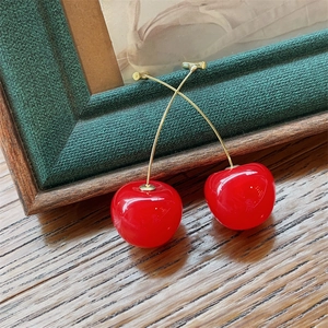 Close-up of bright red cherry earrings with gold stems resting on a green frame