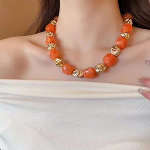 Close-up of chunky orange resin beads and irregular gold metal beads on a fashion necklace