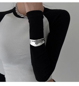 Detail of silver irregular wide open cuff bracelet worn over a knit sleeve