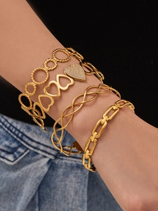 Detail view of stacked gold bracelets featuring heart charms and chunky chain links