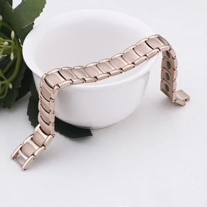 Detail of rose gold magnetic therapy bracelet with linked segments on a white ceramic edge