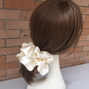 Macro shot of large smooth champagne satin scrunchie on a ponytail for elegant hair styling
