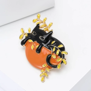 Macro shot of an enamel black cat brooch holding an orange on golden branches