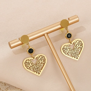 Détail de boucles d'oreilles cœur en acier titane doré avec perle noire sur socle
