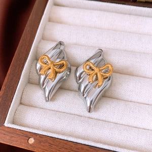 Close-up of silver textured rhombic earrings with gold bow detail in a velvet jewelry box
