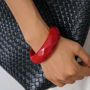 Close-up of a wide red acrylic resin faceted geometric bangle on a wrist over black fabric