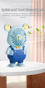 Cute cartoon bear desktop fan with golden bow and blue strap design on stony surface