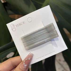 Set of two rectangular grey hair clips with striped texture and gold labels on display card