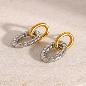 Close-up of interlocking silver twisted and gold smooth hoop earrings on a stone base
