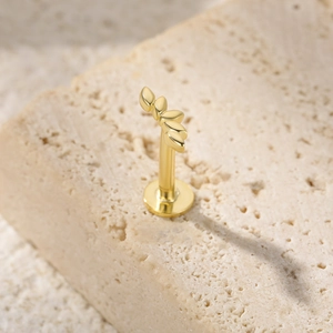 Macro shot of gold five-leaf piercing earring on natural beige stone background