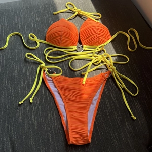 Close-up of orange pleated bikini fabric featuring a gold-toned heart-shaped metal connector