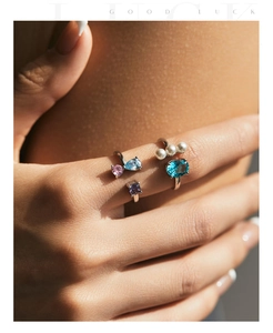 Detail of stacked S925 silver rings featuring blue crystals and pearls in natural sunlight