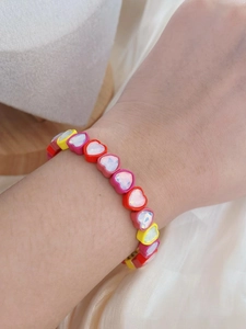 Close-up of a colorful enamel heart-shaped elastic bracelet on a wrist.