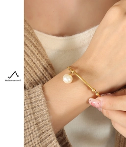 Detail of a gold stainless steel open bangle with a large round pearl on a model wrist