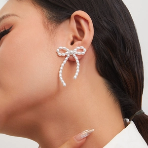 Detail view of a French style bow earring with white pearls worn by a model