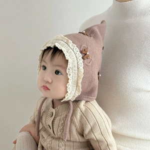 Detail of baby knit bonnet with cream lace trim and brown bow accent with pearl