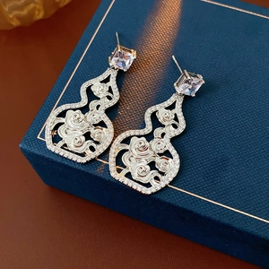 Detailed view of silver hollow gourd earrings with zircon stones on a blue jewelry box