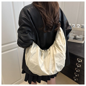 Detail view of large cream dumpling bag featuring pleated texture and double zippers