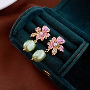 Detail of flower earrings with pink enamel petals and green baroque pearl on velvet