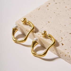Irregular gold U-shaped titanium steel earrings with white pearls on a stone base