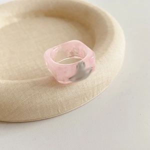 Macro shot of pink resin square ring featuring metallic Saturn orb detail on textured tray