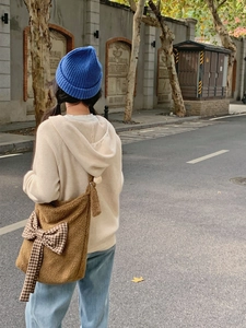 Detail of a brown fuzzy crossbody bag with a plaid ribbon bow on a street style model