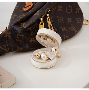 Detail of a white round mini jewelry box with golden zipper showing a pearl ring inside