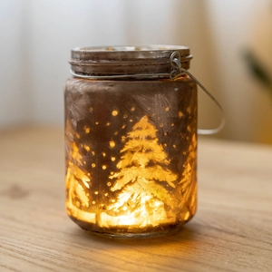 Christmas glass candle holder with pine tree silhouette and warm LED light on wood table