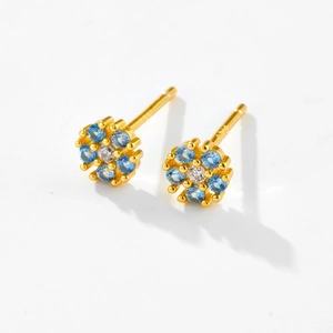 Macro shot of gold flower earrings with a white center stone and blue petals