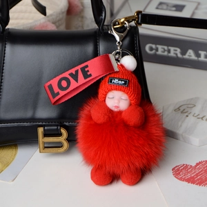 Detail of red fox fur puff keychain with sleeping doll on a black designer handbag