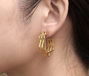 Close-up of golden multilayer geometric hoop earrings worn to show modern metallic texture
