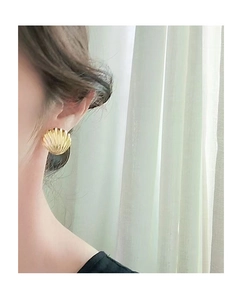 Close-up of elegant gold shell earring worn by a model against soft natural lighting
