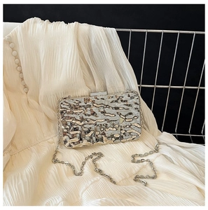 Detail of silver metallic clutch featuring wave pattern texture and silver chain strap