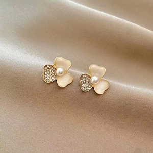 Macro shot of three-petal flower stud earrings with pearls and crystals on silk
